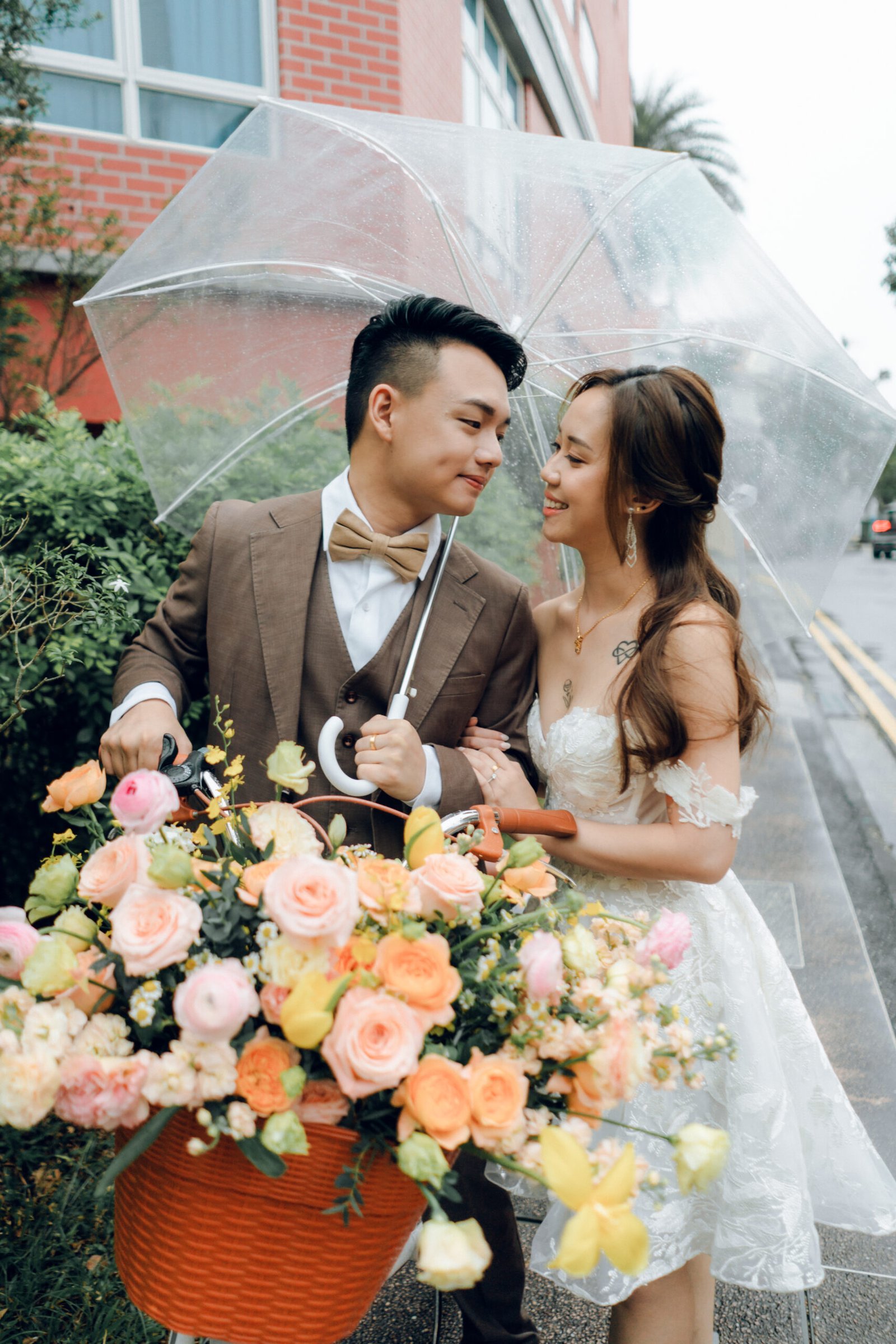 Couple beneath a clear umbrella carrying peach and coral flowers