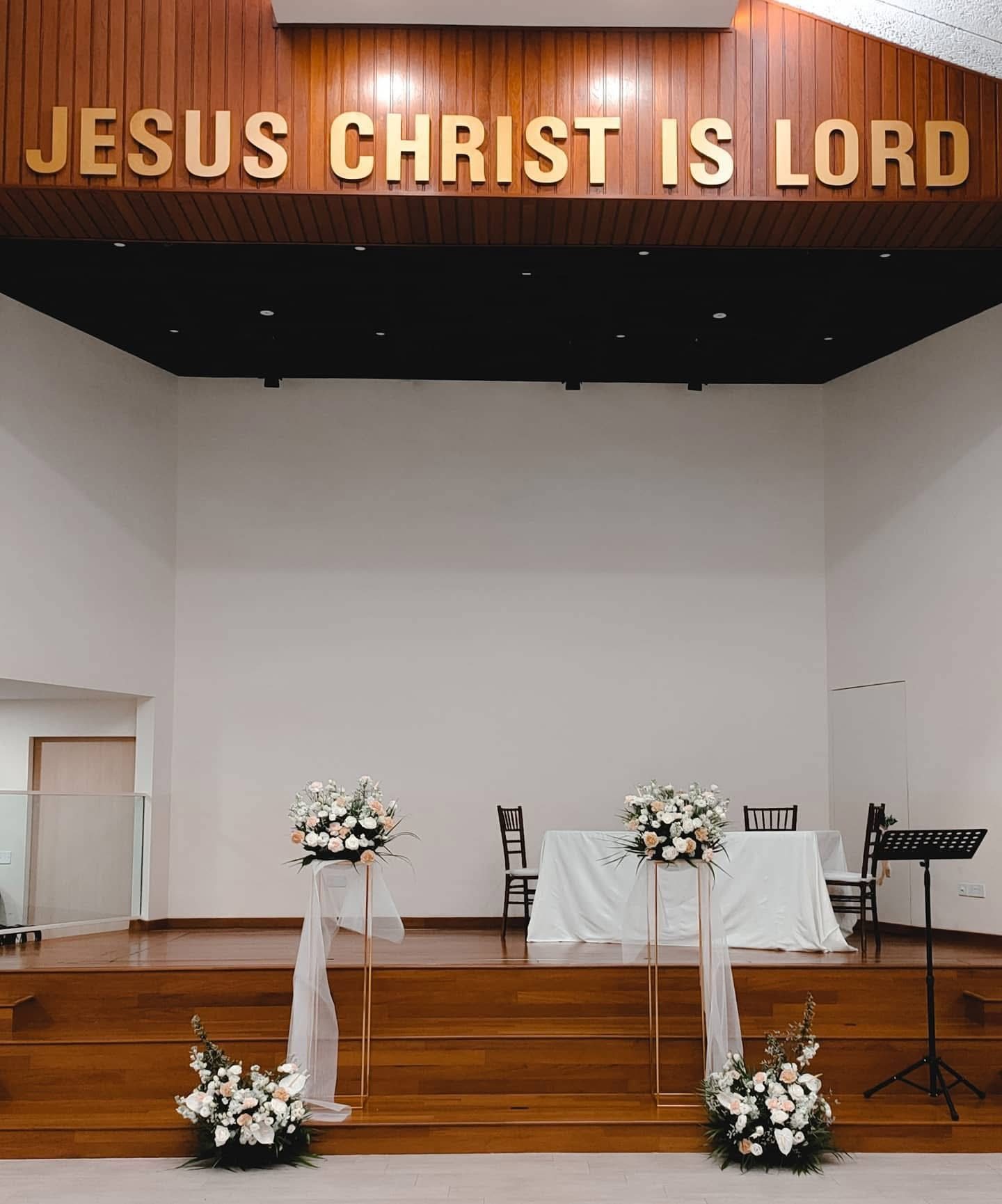 Ceremony stage with gold stands draped in tulle, white and blush flowers and wooden paneling above