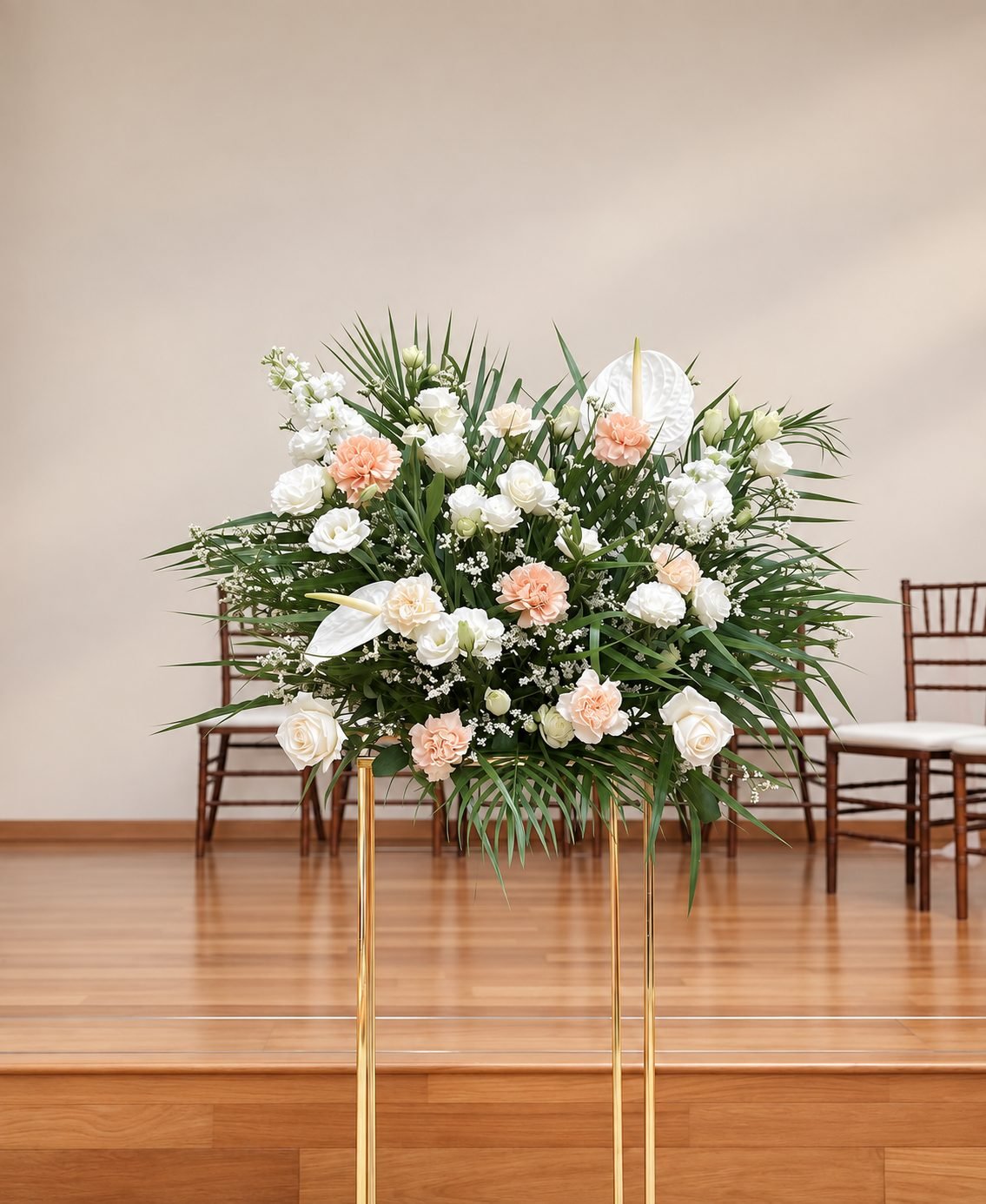 White and blush floral arrangement with green palm foliage on a tall gold stand