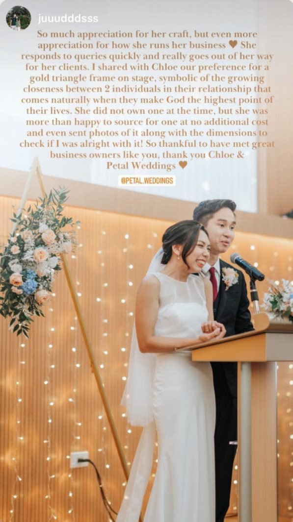 Couple at a podium during a ceremony, with a triangular floral frame and warm string lights behind them