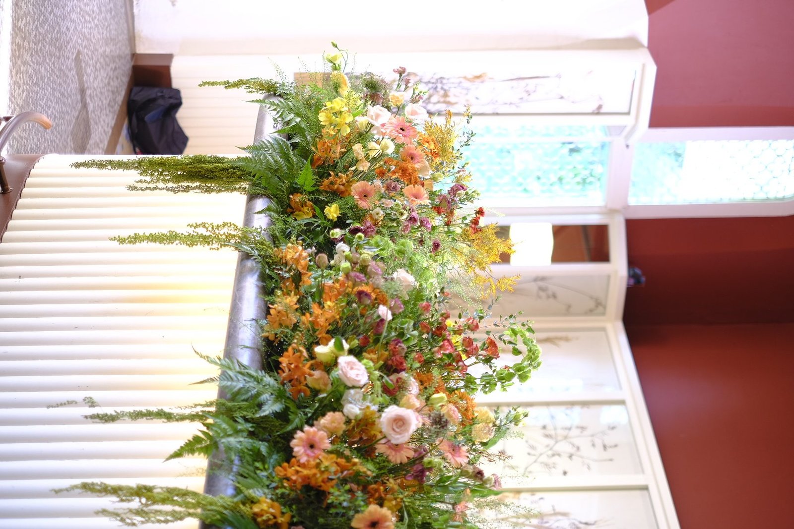 Long abundant floral arrangement in apricot, pink and green spilling along a white bar counter