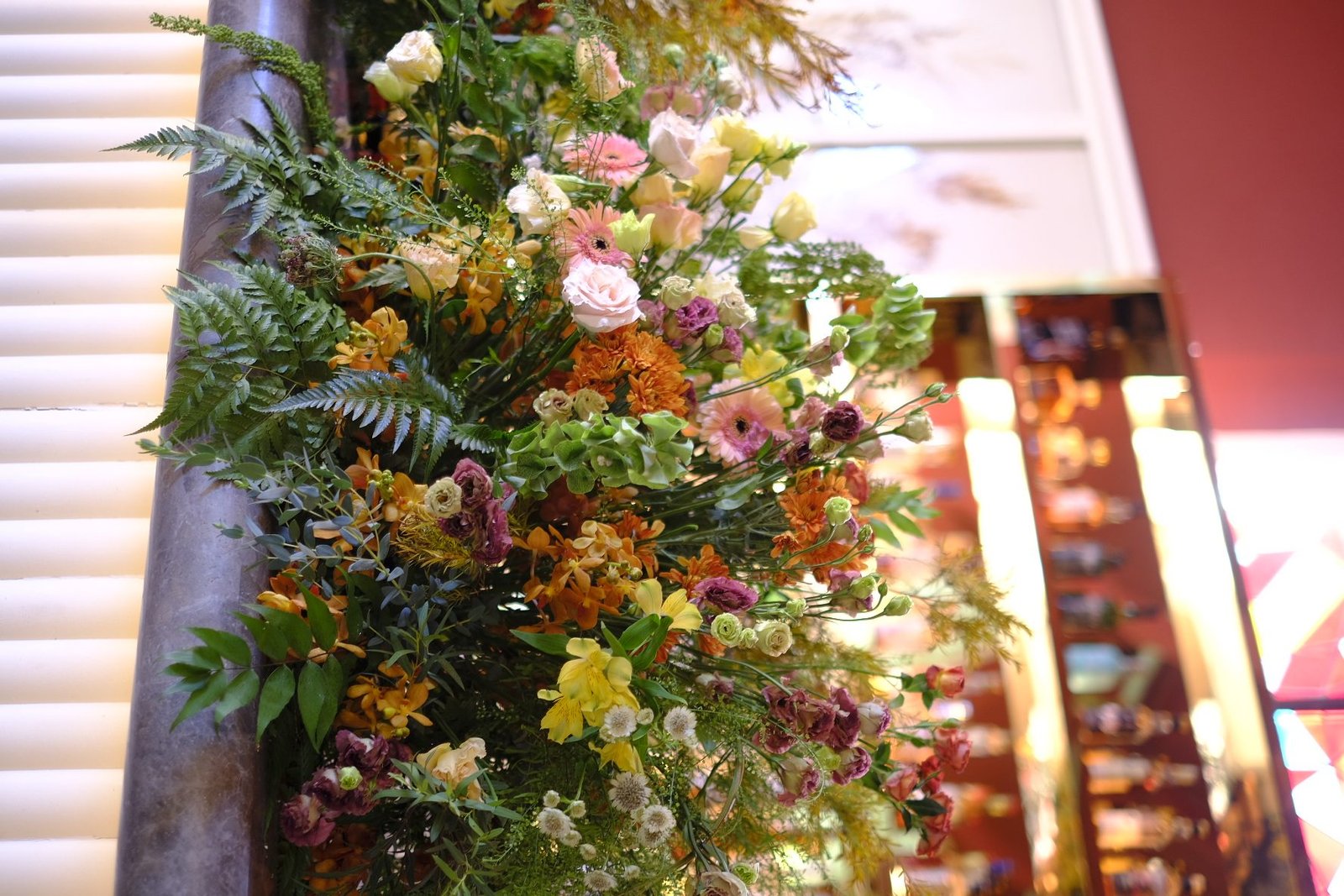 Close detail of layered pink, orange and yellow blooms with ferns against a marble column