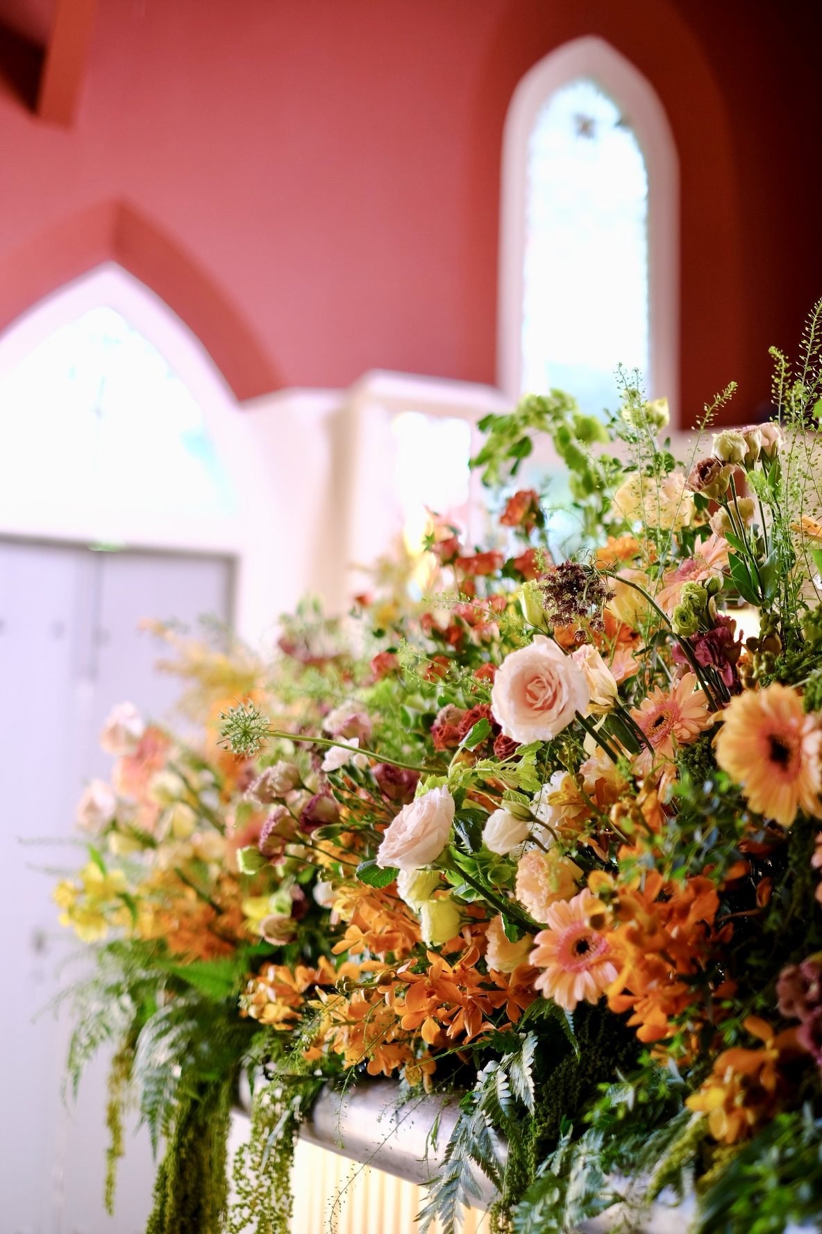 Abundant pink and orange arrangement against terracotta walls and arched windows