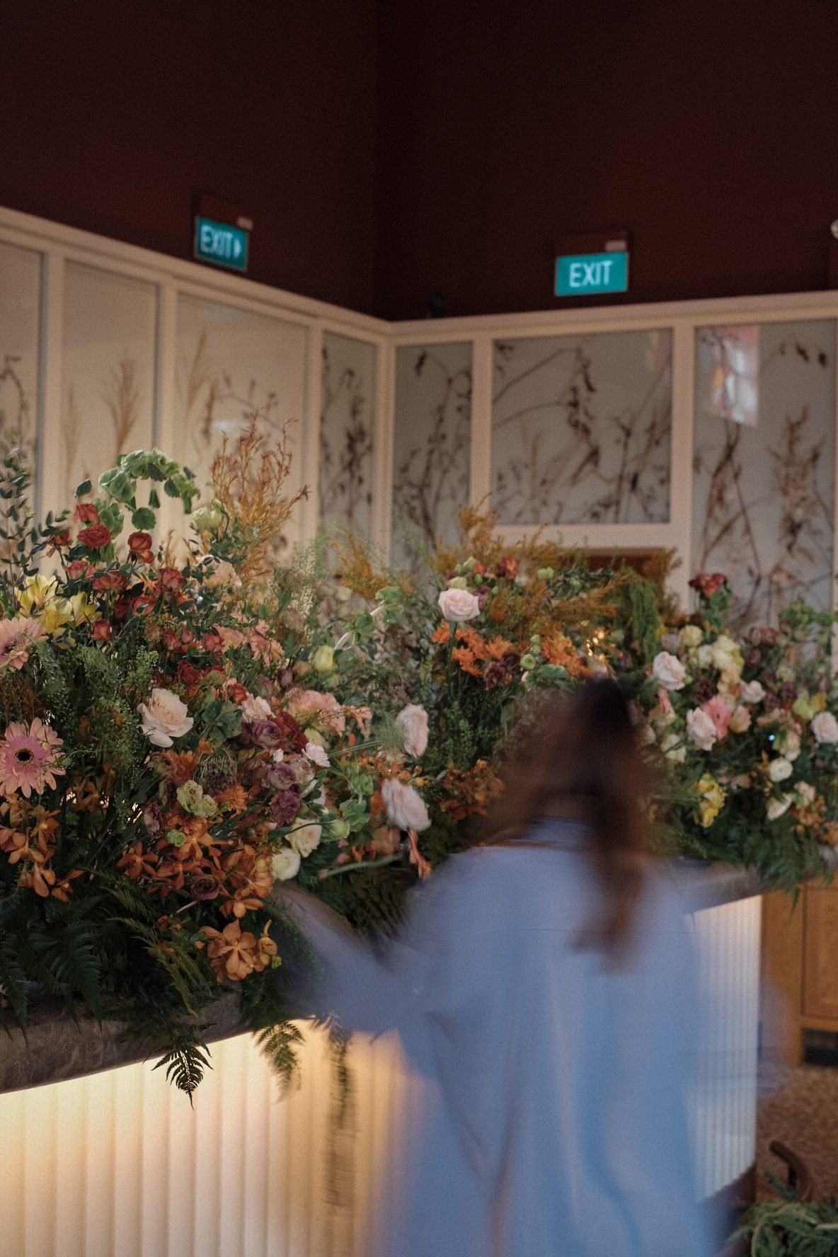 Long bar floral installation of warm layered flowers seen from the dining side