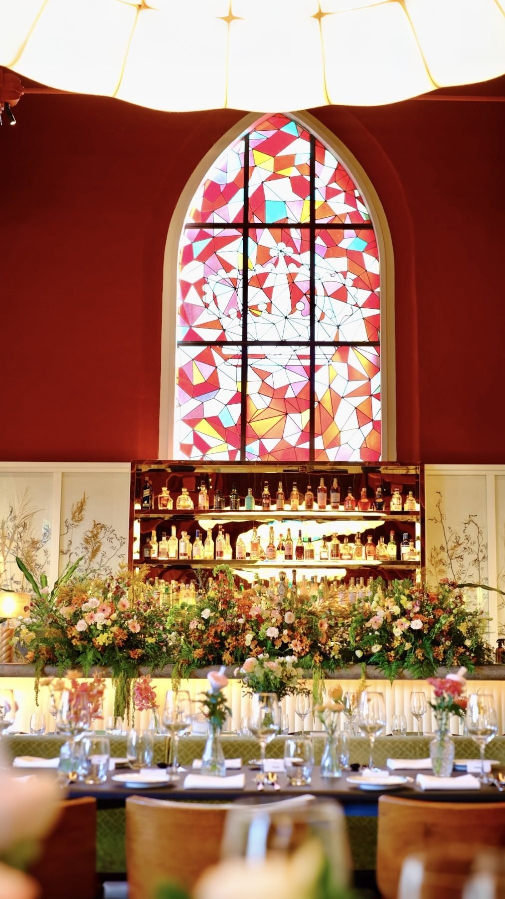 Restaurant bar with a long floral arrangement beneath a colourful arched stained-glass window