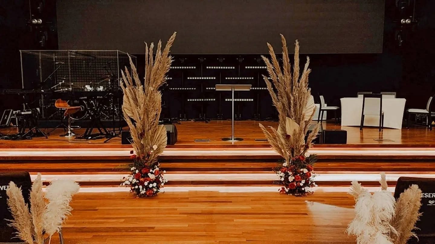 Tall pampas grass arrangements with small red and white flowers flanking the dark stage