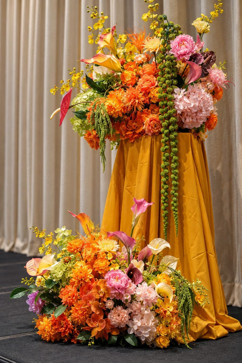 Close-up of a tall pedestal arrangement with orange dahlias, pink peonies and hanging green bead strands