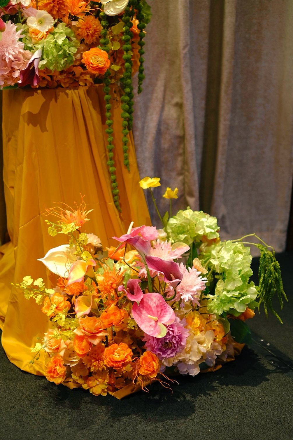 Loose floor arrangement at the base of a mustard pedestal with orange, pink anthurium and green hydrangea