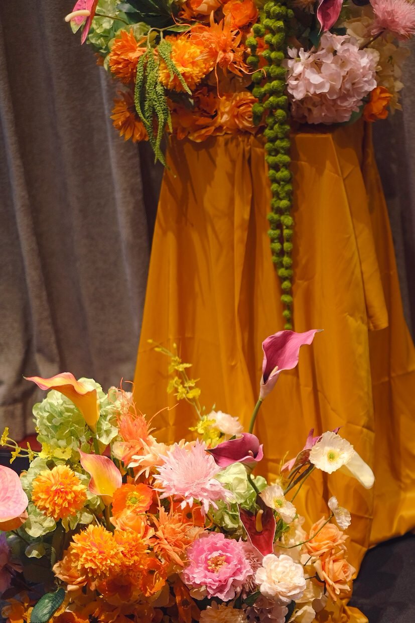 Close view of a pedestal and floor arrangement with orange, pink and yellow flowers
