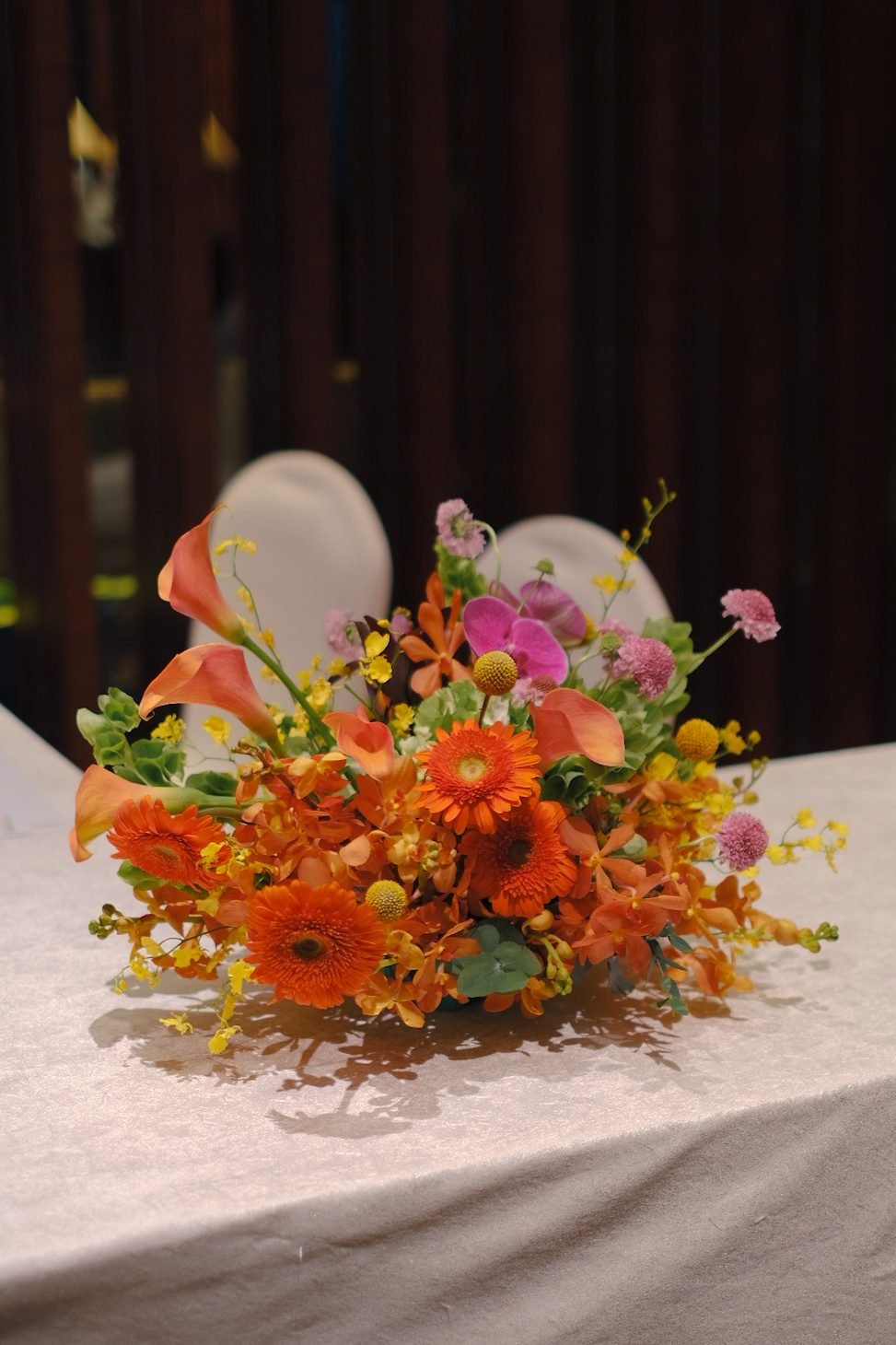 A bright orange, fuchsia and yellow arrangement on a white linen reception table