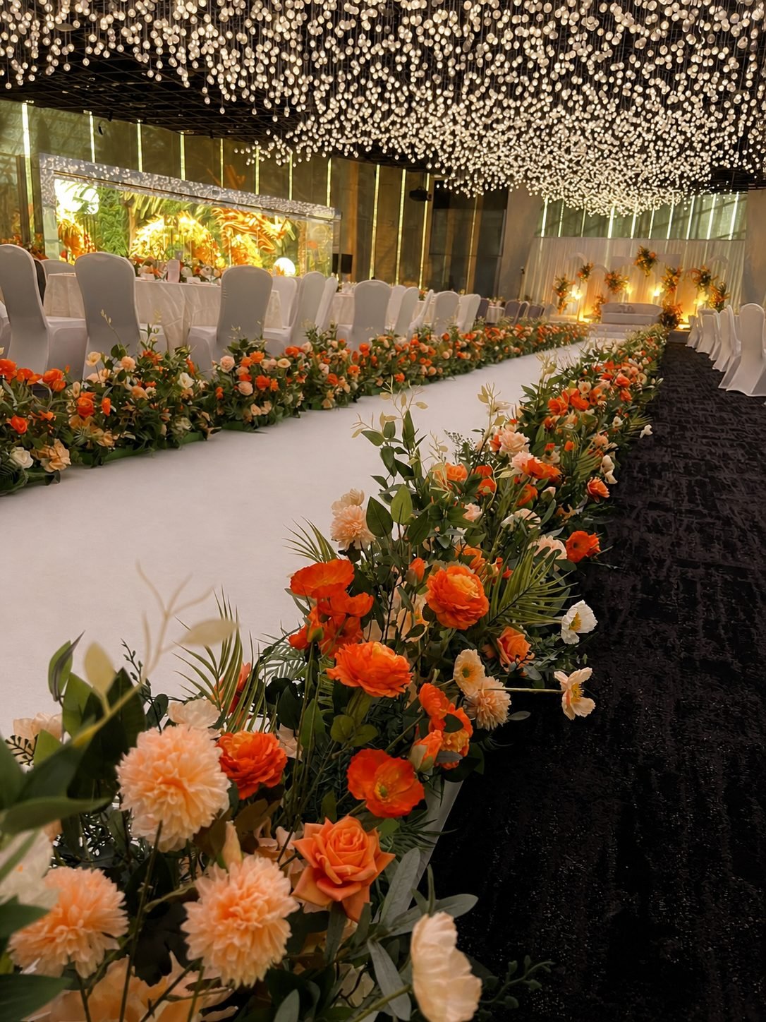 Long low floral border in warm orange and peach lining an aisle between rows of chairs