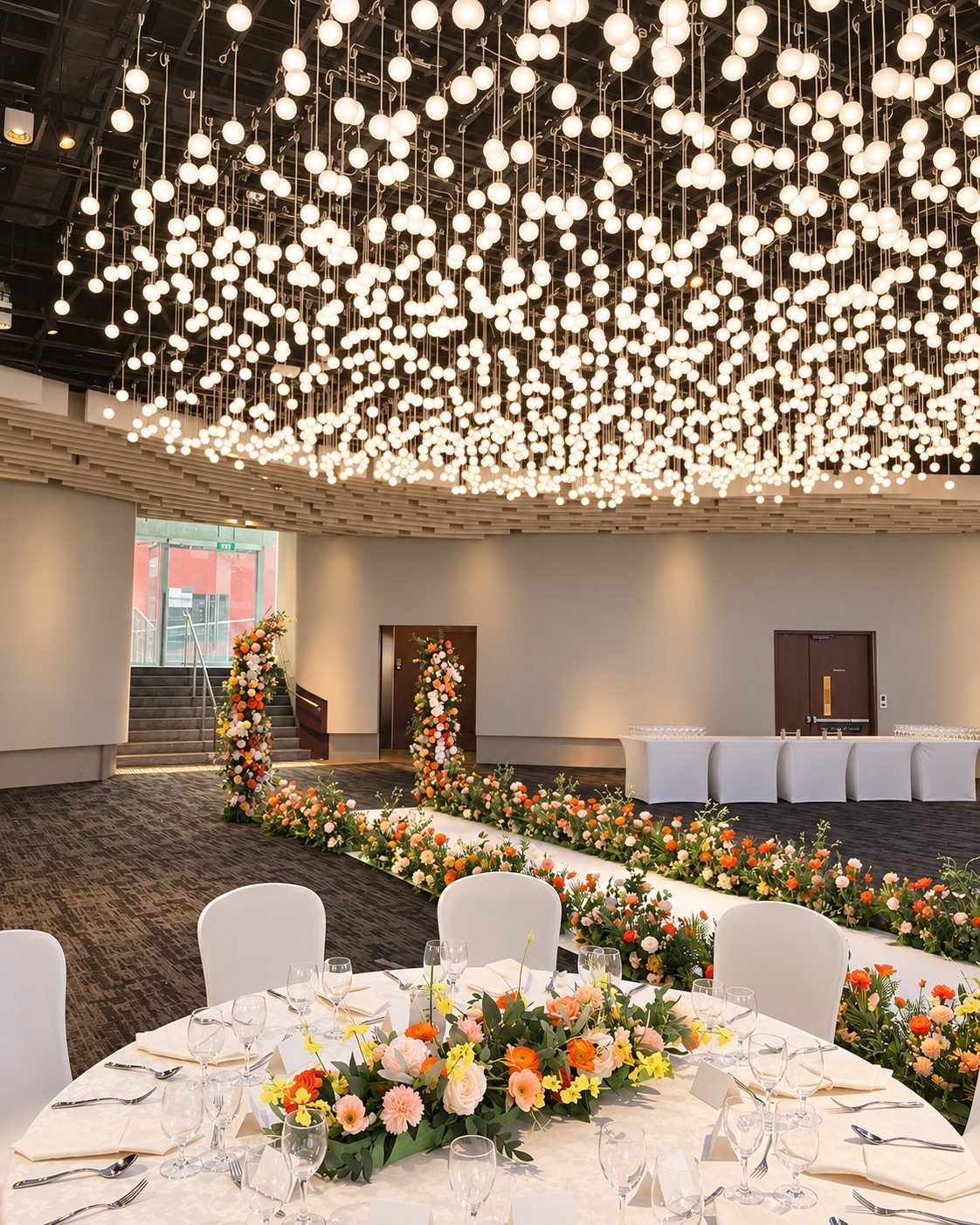 Banqueting hall with hanging globe lights, a round reception table and floral aisle pillars