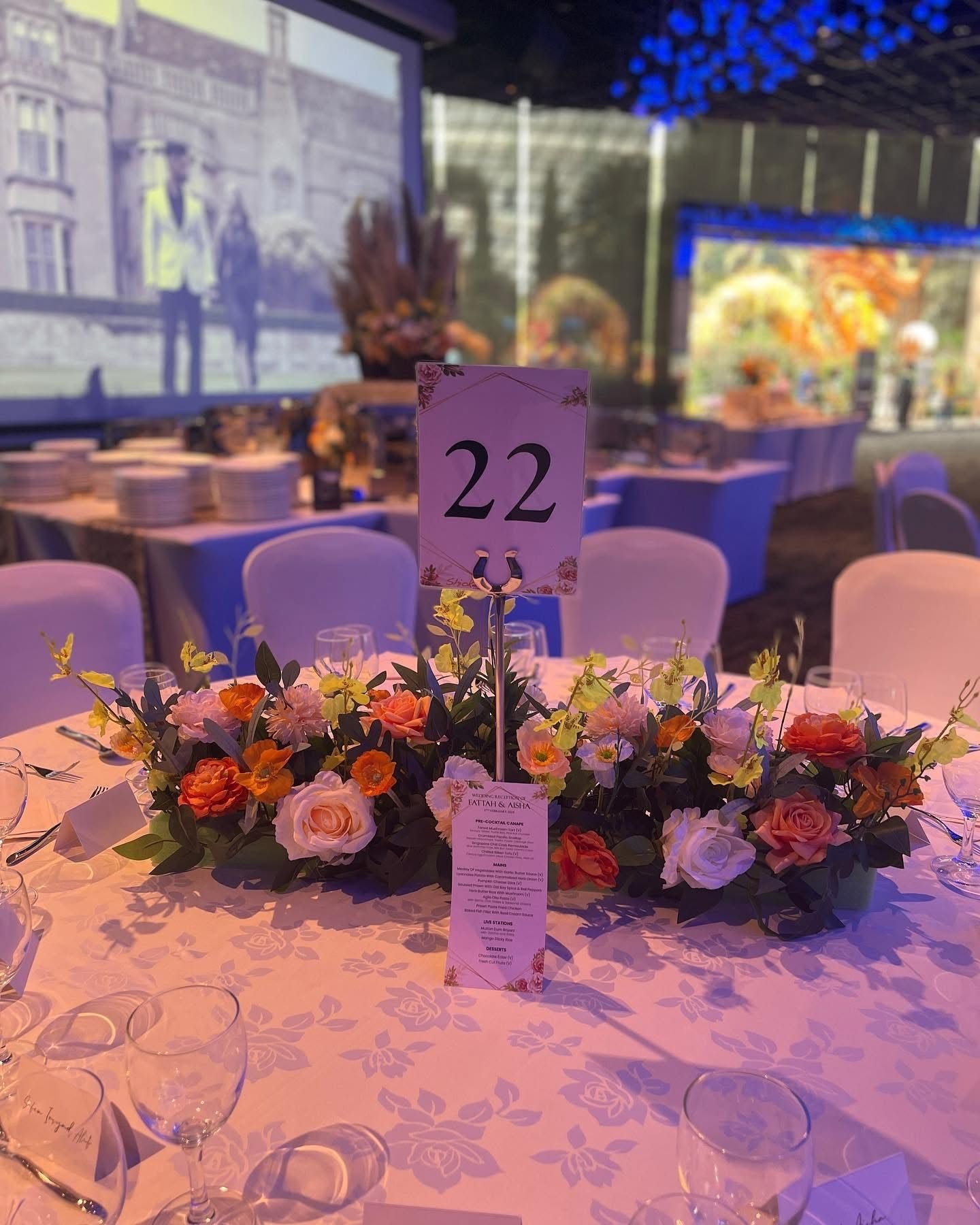Round reception table with a low orange and peach floral centrepiece and table number