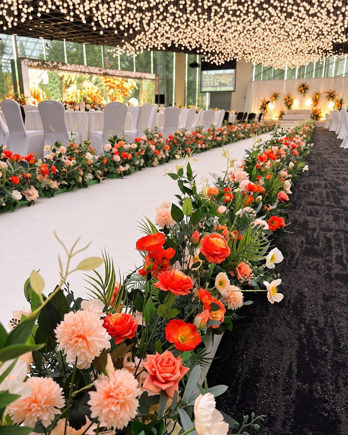 Low orange, peach and rose floral border lining a long white ceremony aisle