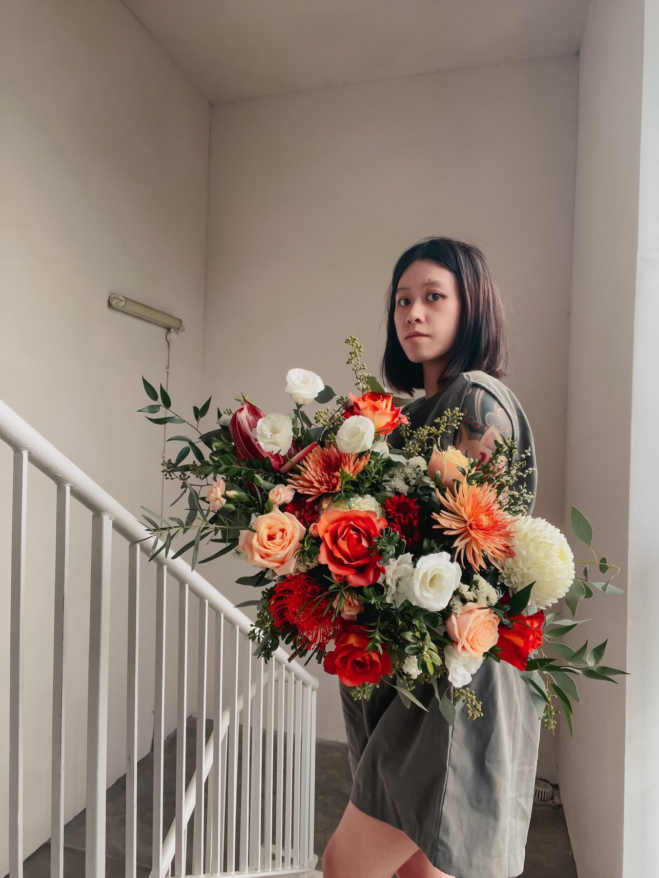Large bridal bouquet of orange, rust, peach and white blooms held on a staircase landing