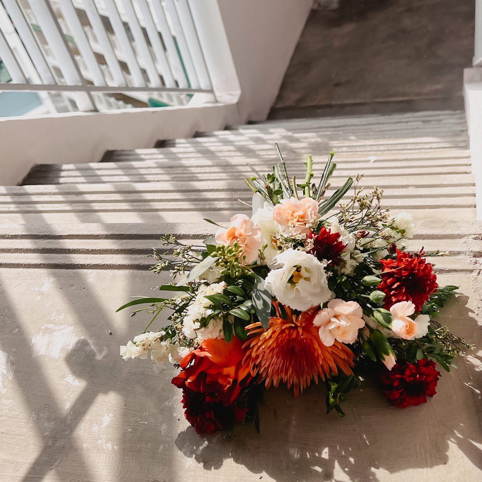 Peach, white and rust bridal bouquet resting on sunlit concrete steps