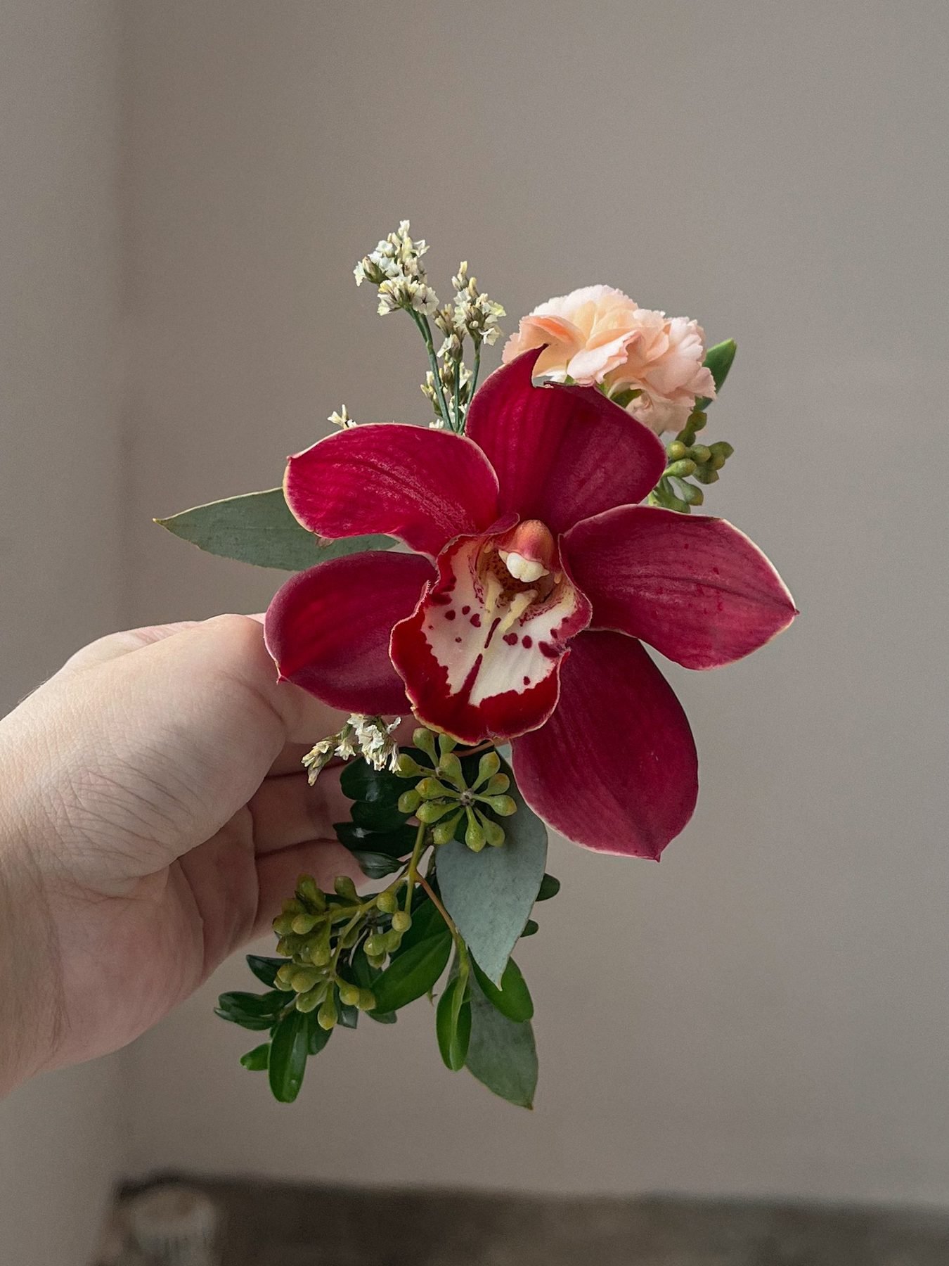Close-up of a burgundy orchid boutonniere with a peach carnation and greenery