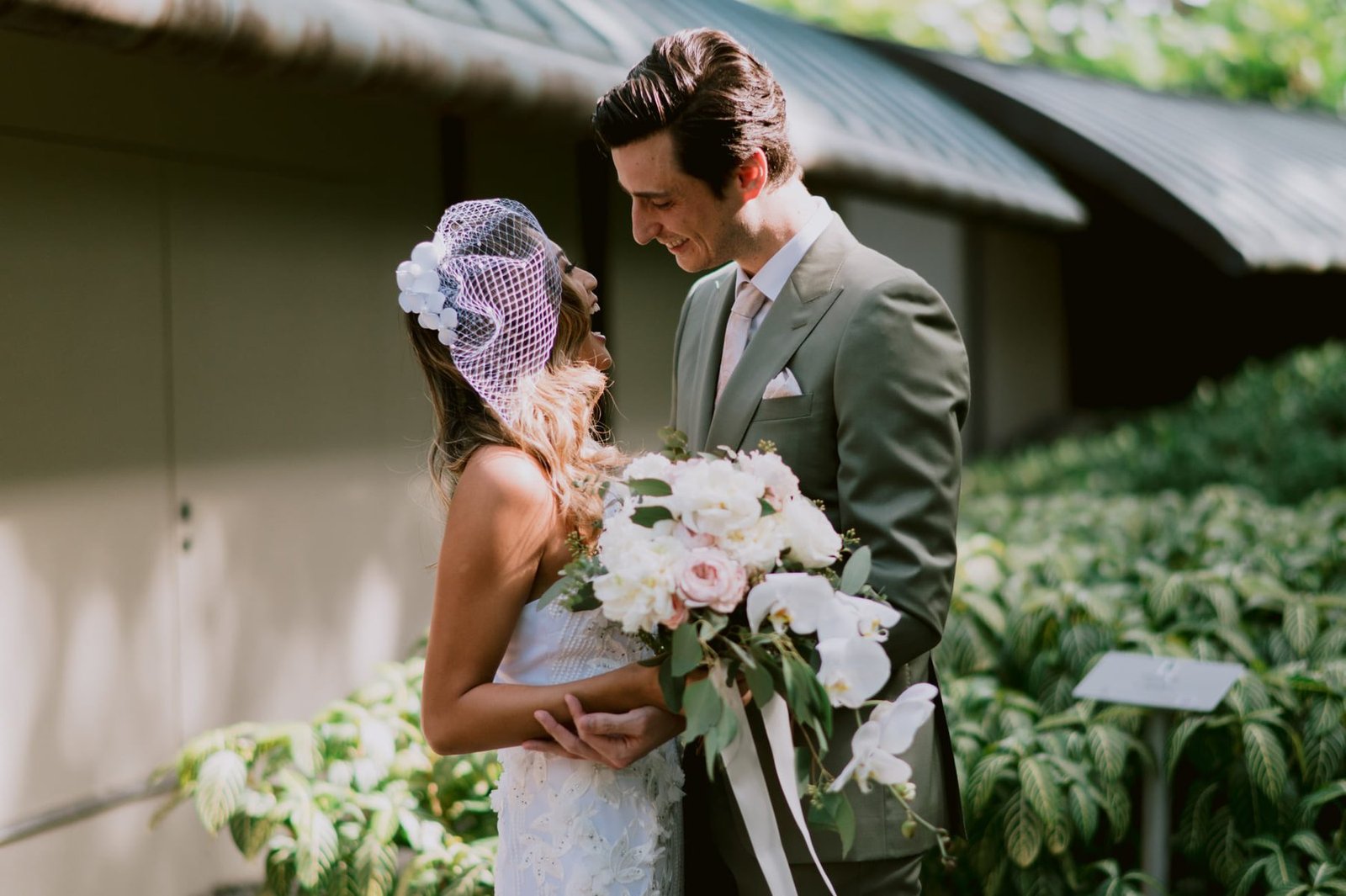 Bride and groom close together, the bride holding a blush and white cascading bouquet with orchids