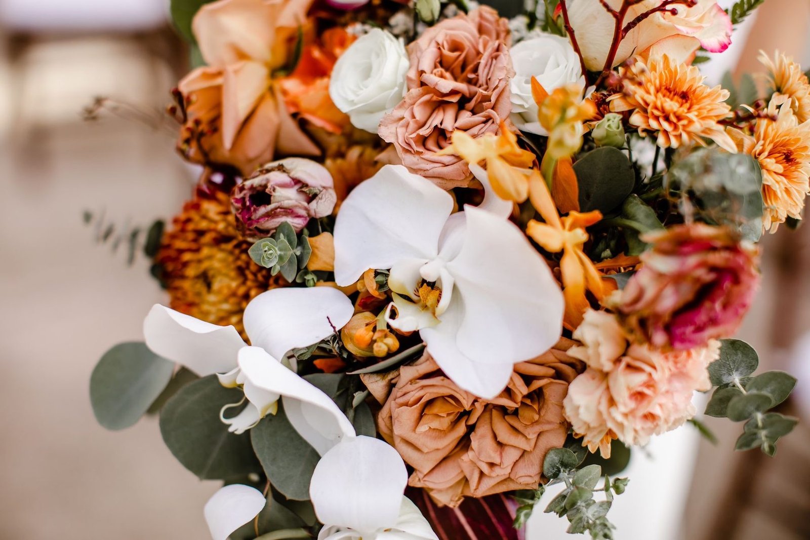 Close detail of a bouquet with white orchids, blush roses and orange dahlias among eucalyptus