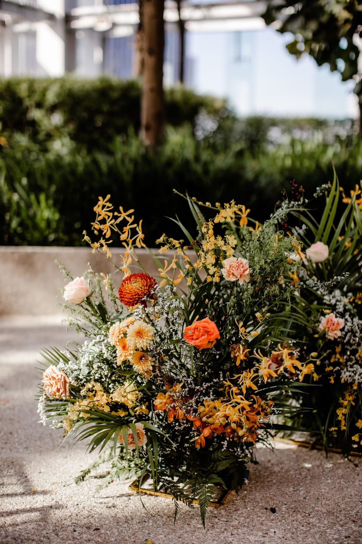 Free-standing arrangement of yellow and orange orchids, pink roses and greenery on a rooftop