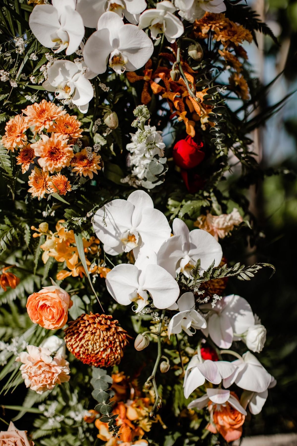 Close detail of a floral pillar with white orchids, orange dahlias, roses and ferns