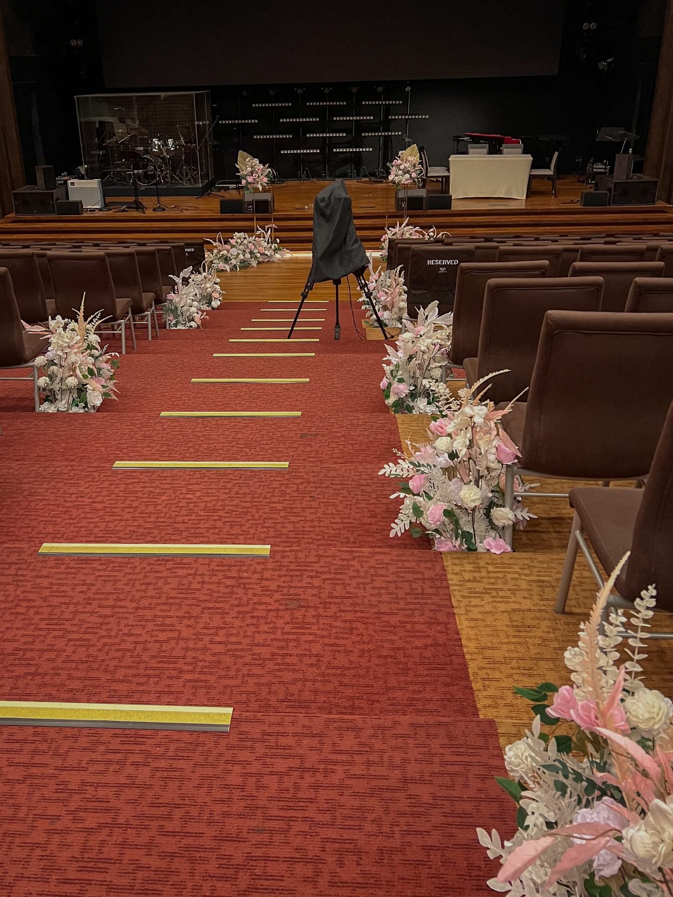 A red-carpet ceremony aisle lined with blush and white floral arrangements between dark chairs