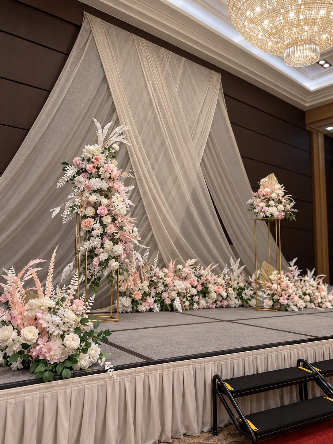Front view of a draped ballroom backdrop with a tall blush and white floral pedestal and floor line