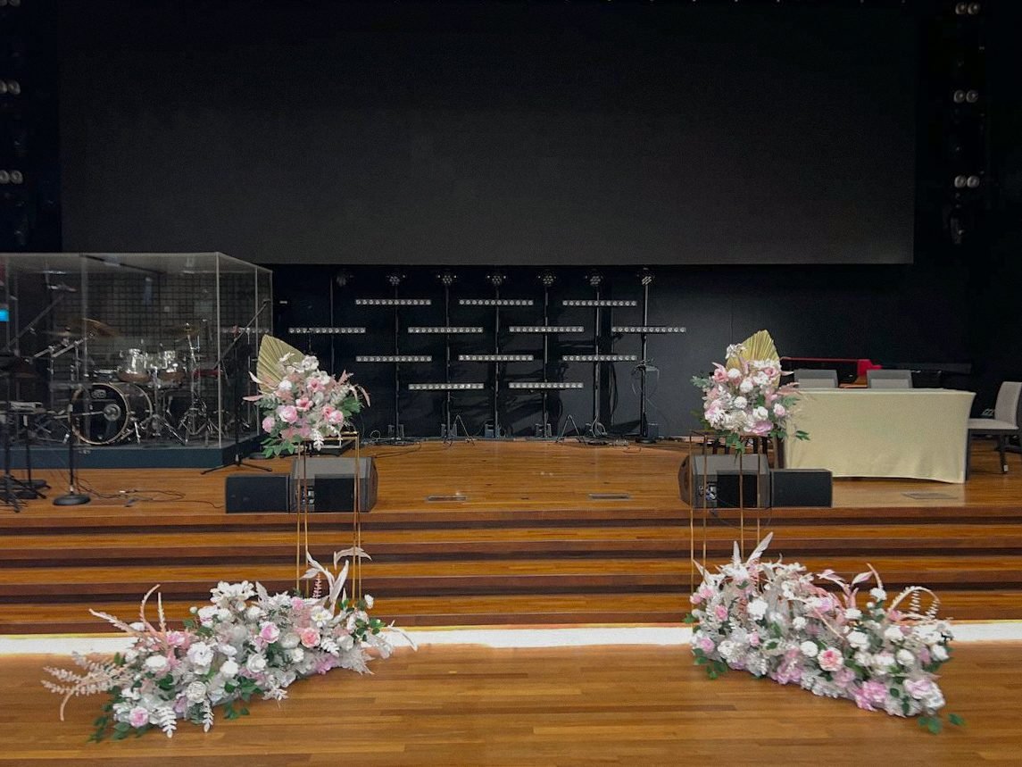 A wooden church stage dressed with blush and white floral pedestals and floor arrangements