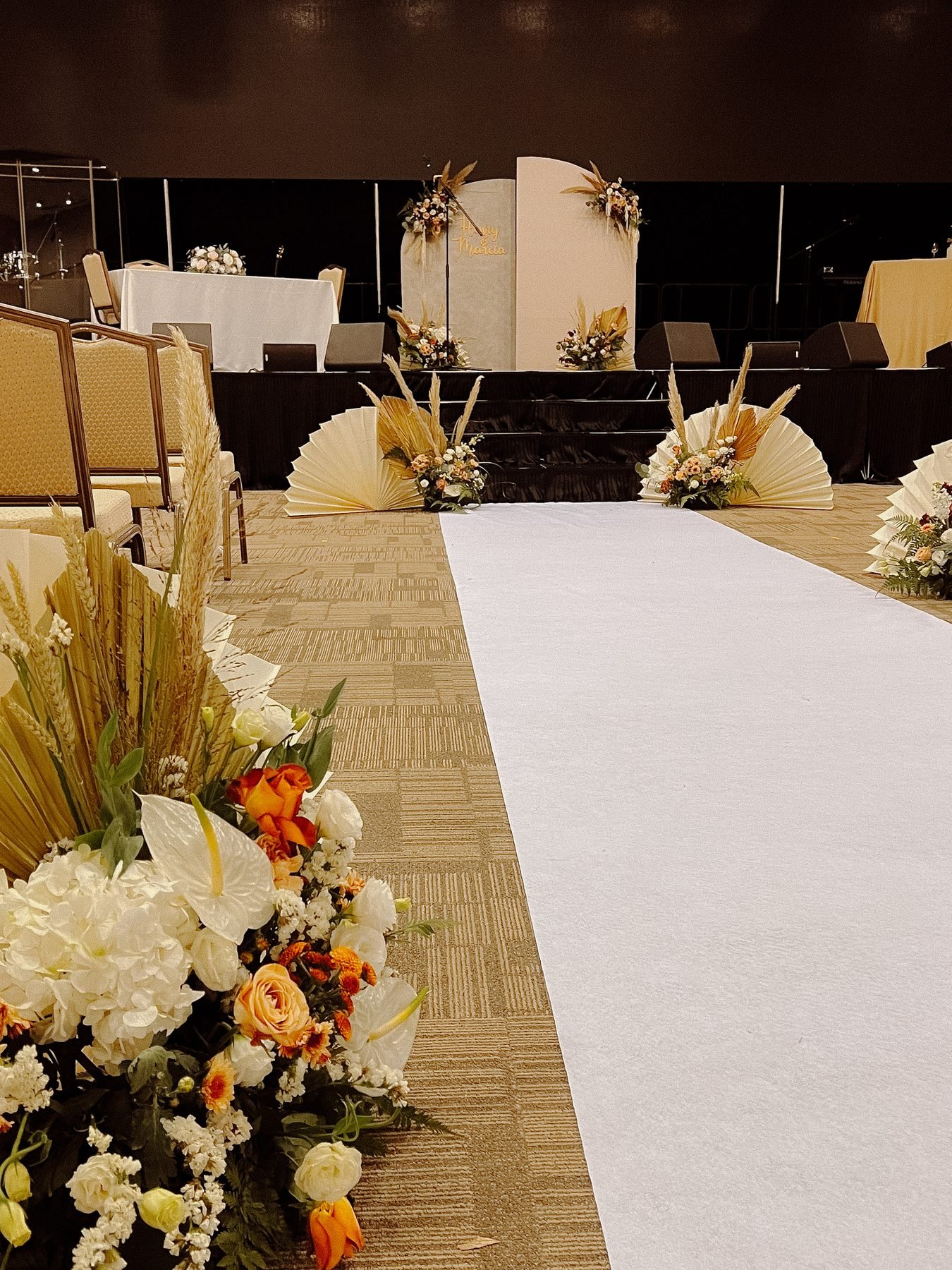 White ceremony aisle leading to a stage backdrop, lined with pampas, pleated fans and floor floral clusters