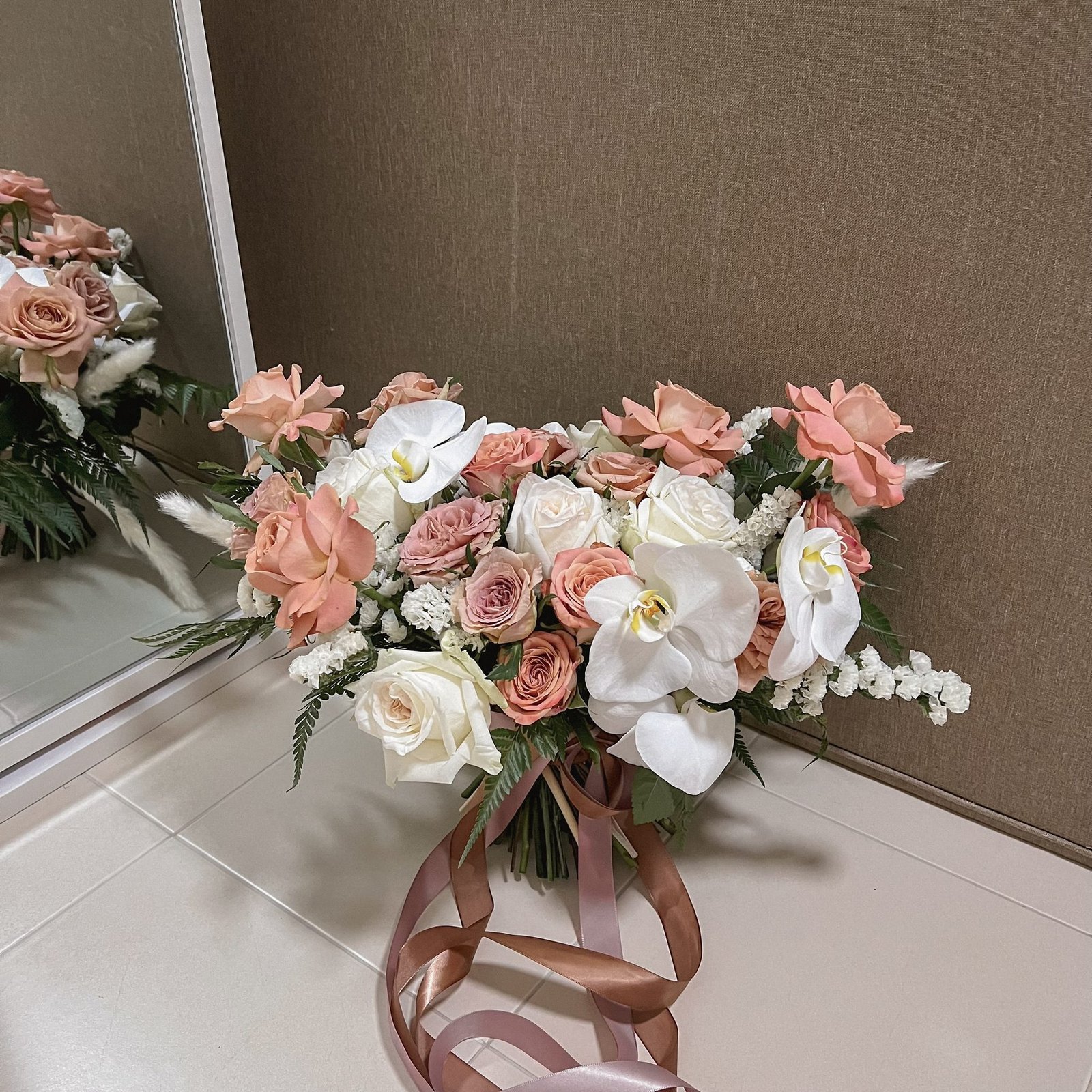 Blush and ivory bridal bouquet with white orchids and trailing ribbons resting by a mirror