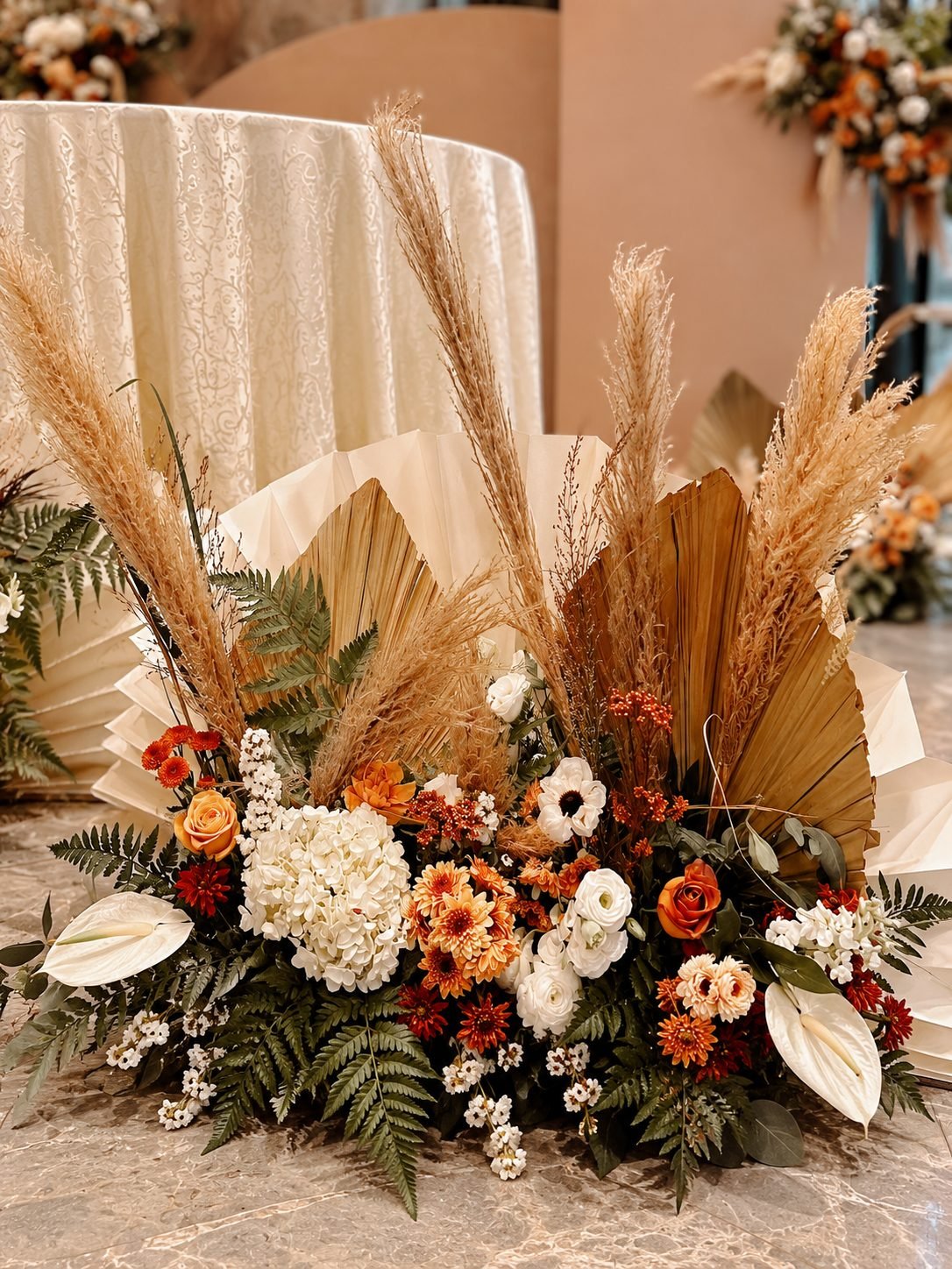 Floor floral cluster of ivory hydrangea, rust roses and pampas against pleated paper fans