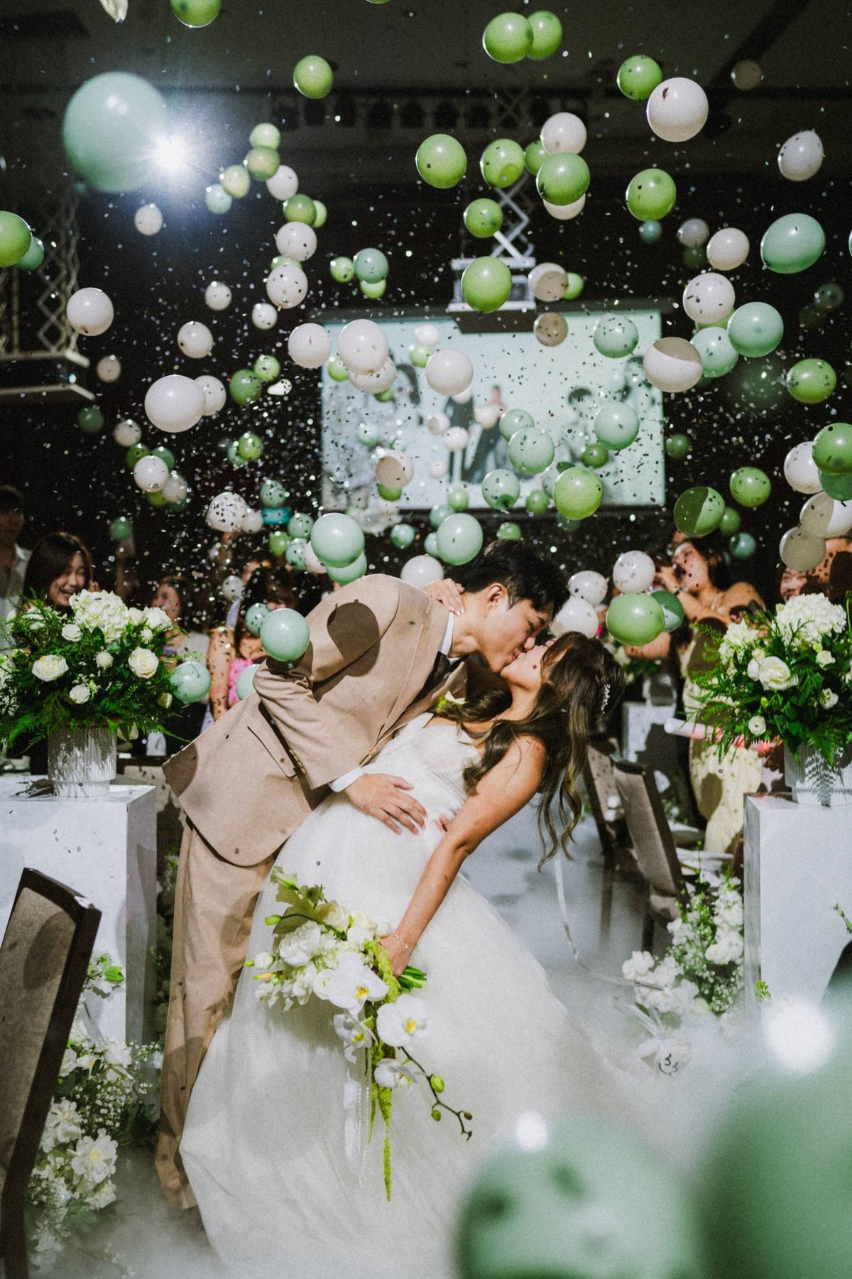 Groom dipping the bride for a kiss as green and white balloons and confetti fall around them