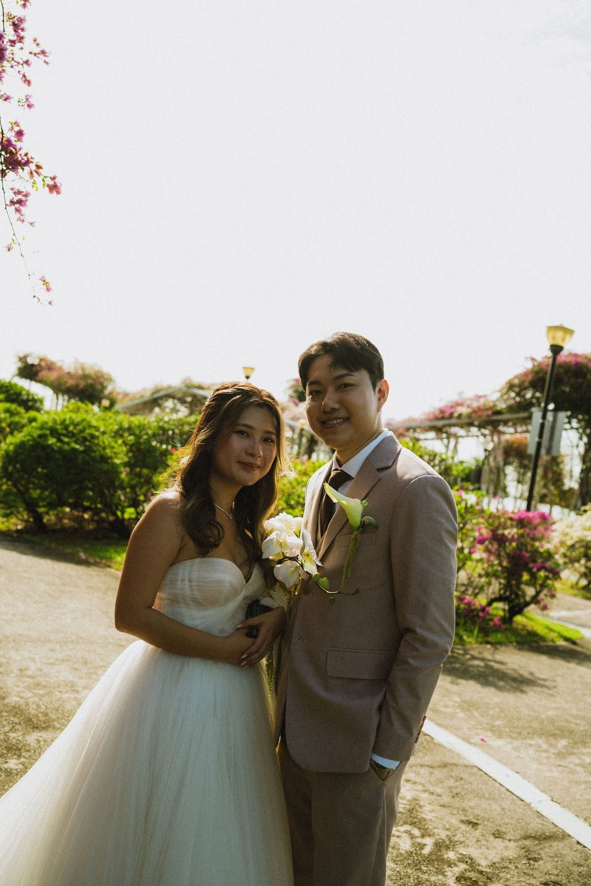 Bride and groom standing together on an outdoor path, the bride holding the white cascading bouquet