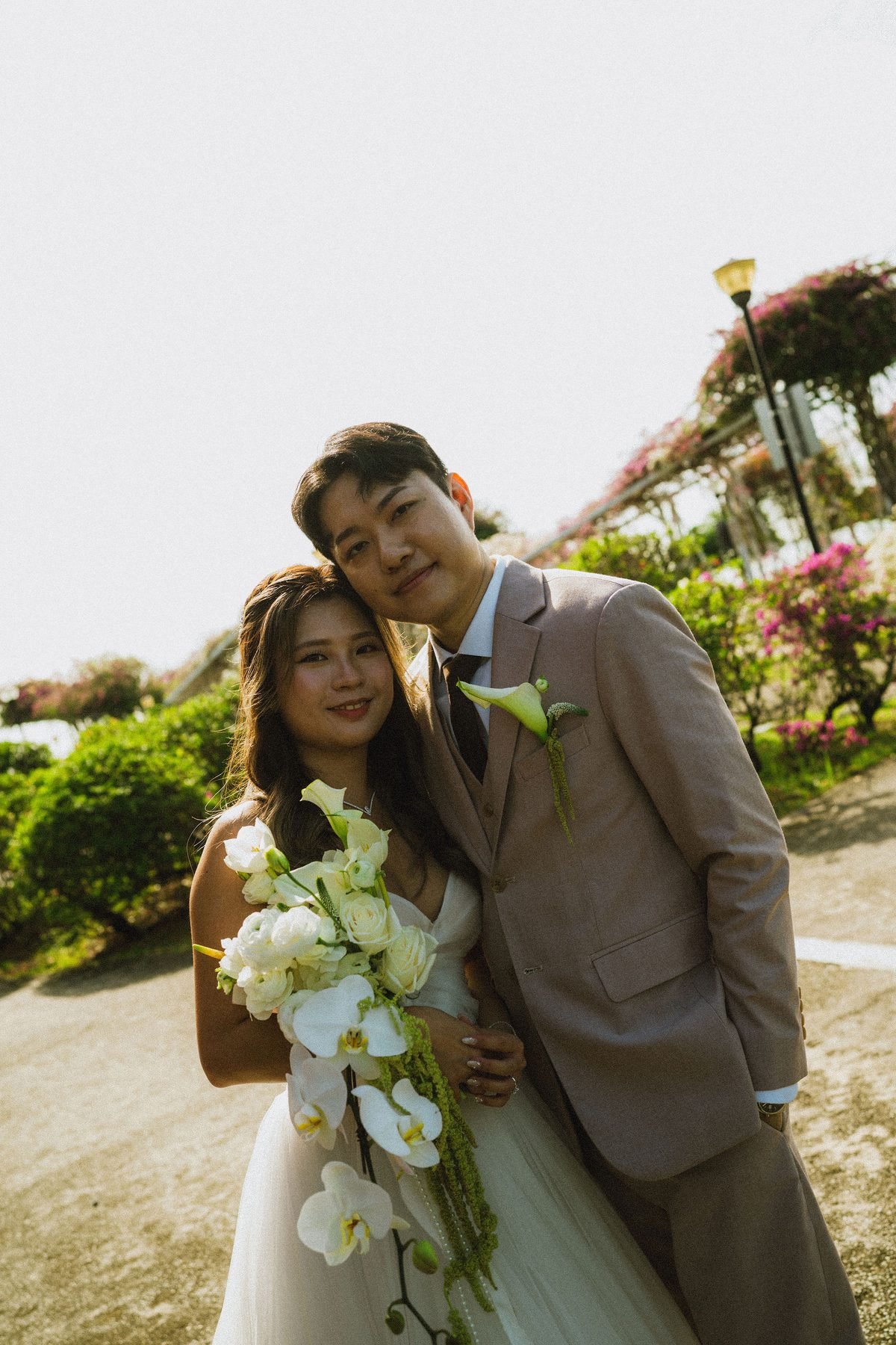 Bride and groom leaning close, the bride holding the white cascading bouquet outdoors