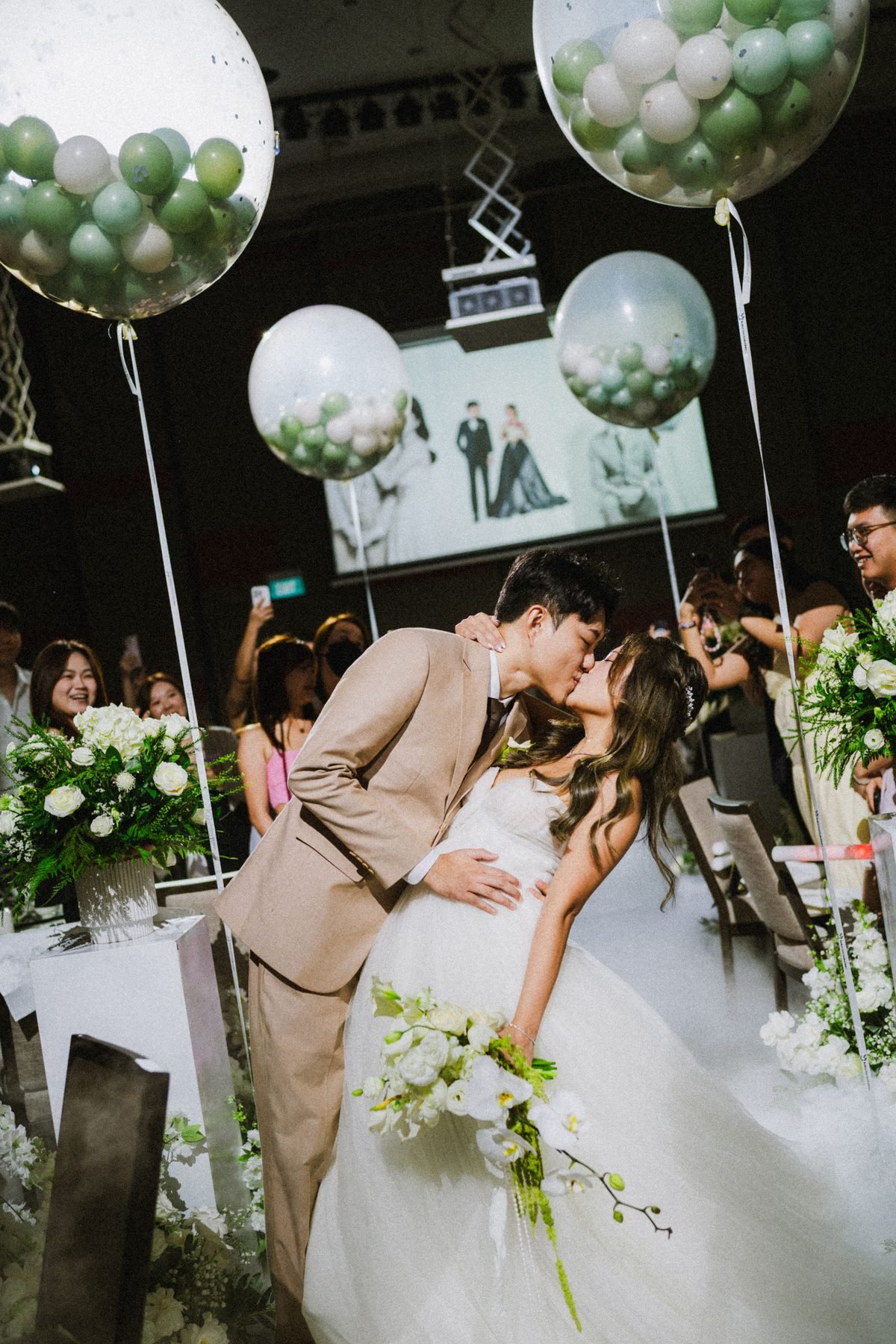 Groom dipping the bride beneath large transparent balloons filled with small green and white balloons