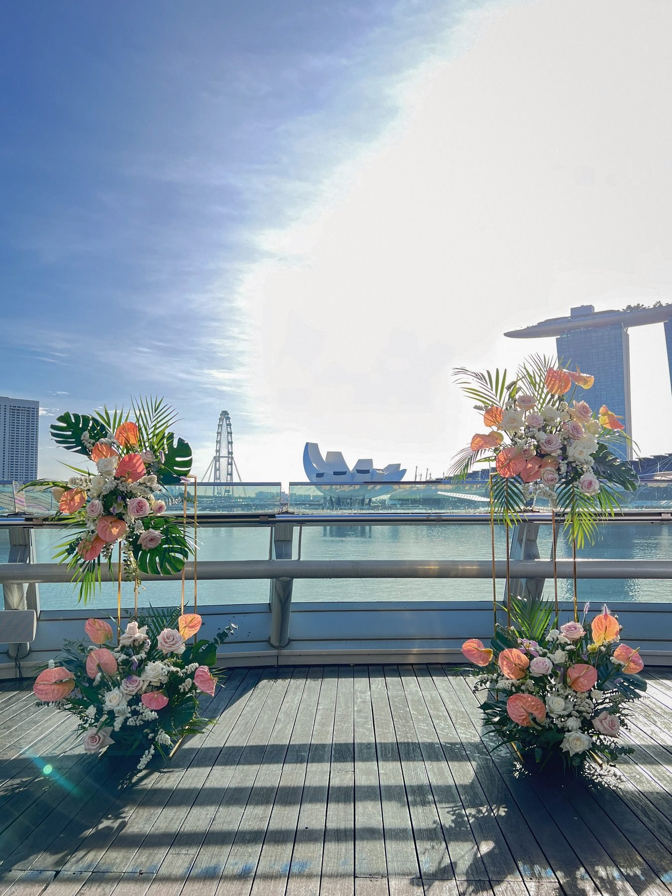 Waterfront ceremony set-up with two tall floral stands and floor clusters overlooking Marina Bay