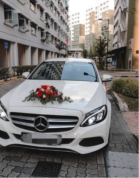 A white wedding car decorated with a red, white and green floral arrangement on the bonnet