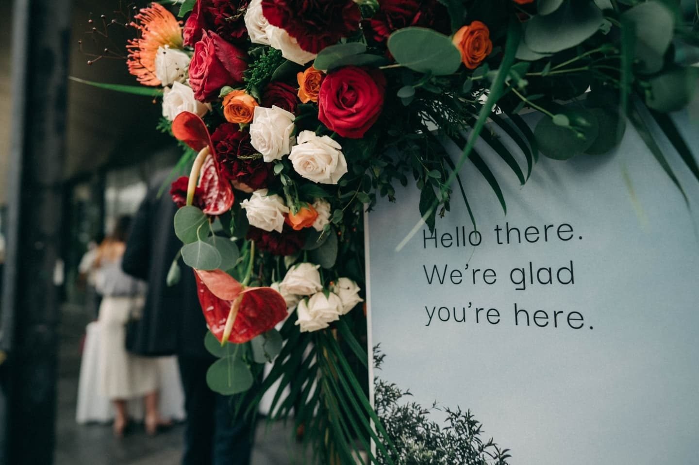 Red, cream and green floral cluster along the edge of a welcome board beside greeting text