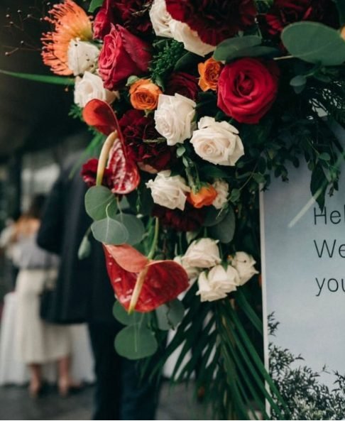 Close detail of a red, cream and green floral cluster arranged along a welcome board