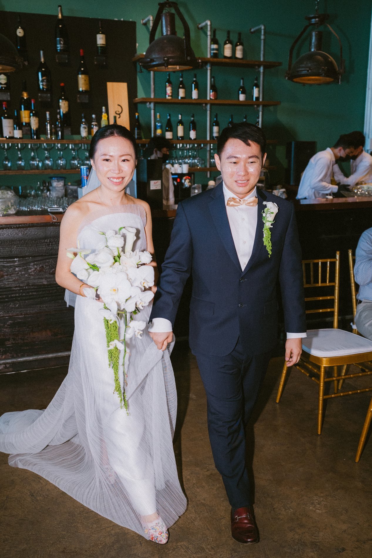 Nic and Zia walking hand in hand through the Cargo 39 bar, the bride holding a white cascading bouquet