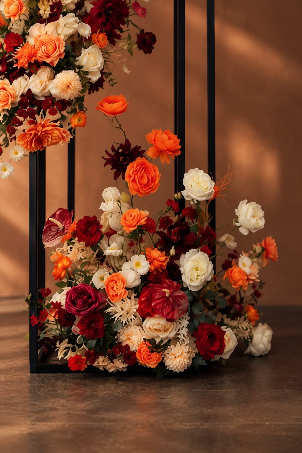 Close detail of a black frame dressed in burgundy, orange and cream roses and anthuriums
