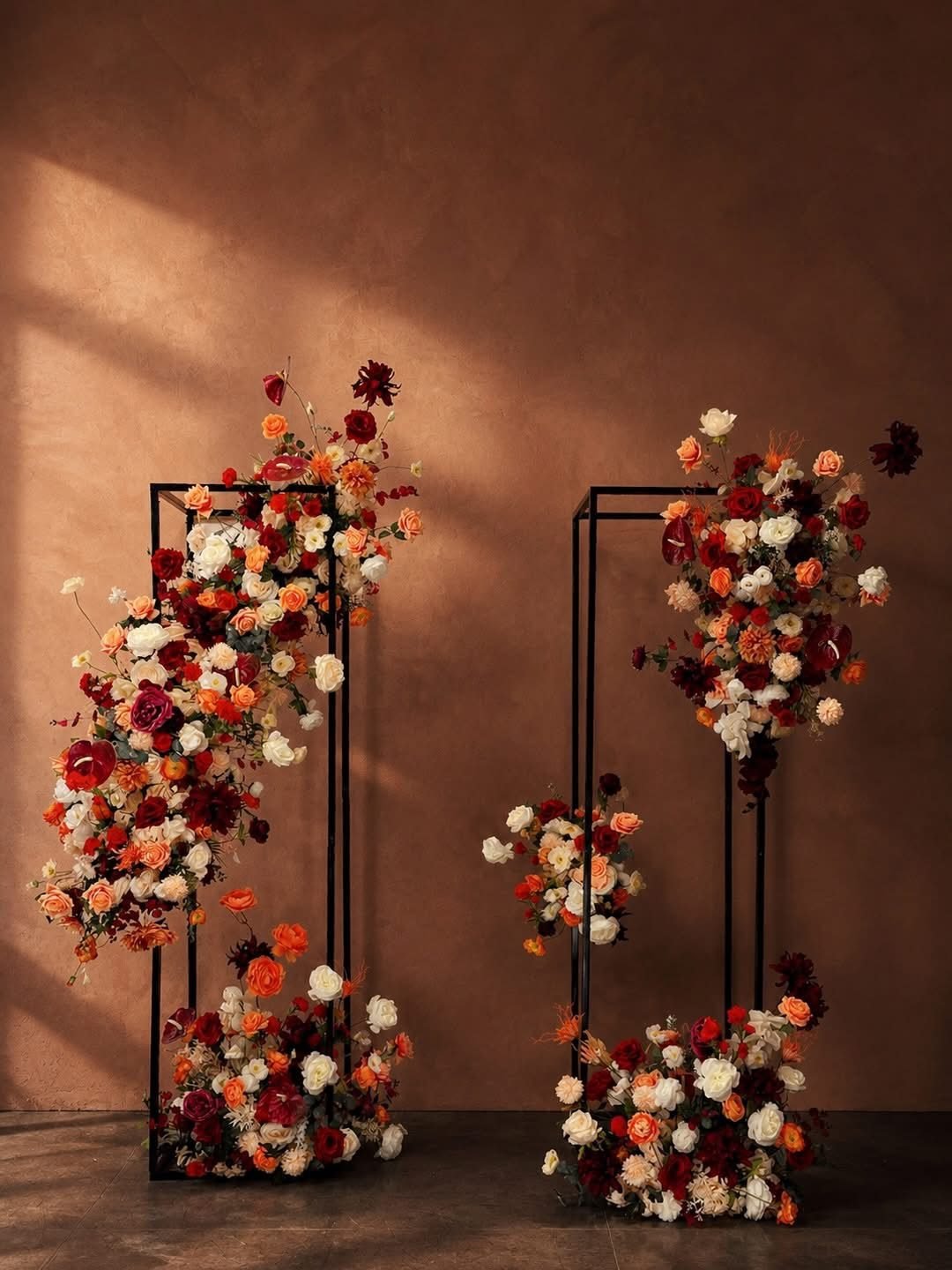 Two black frame stands fully dressed in burgundy, apricot and cream against a warm brown wall