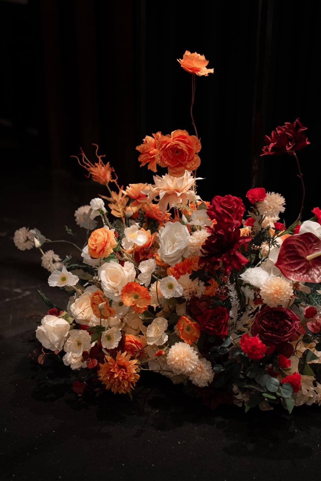 Floor cluster of burgundy, apricot and cream roses and anthuriums against a dark background