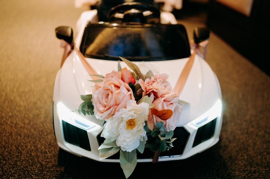 Small white ceremonial car decorated with a peach and white floral arrangement on the bonnet