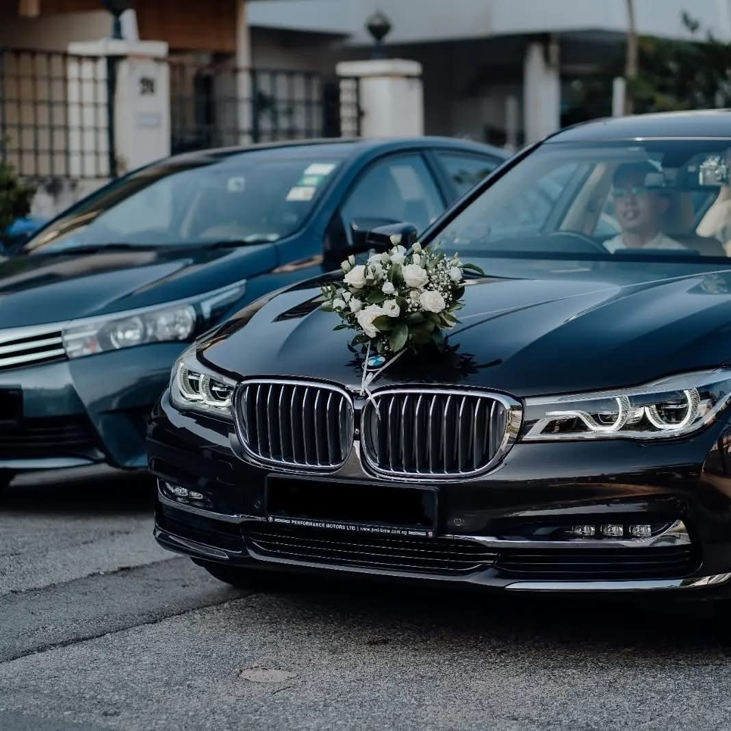 Black wedding car with a small white floral arrangement on the grille