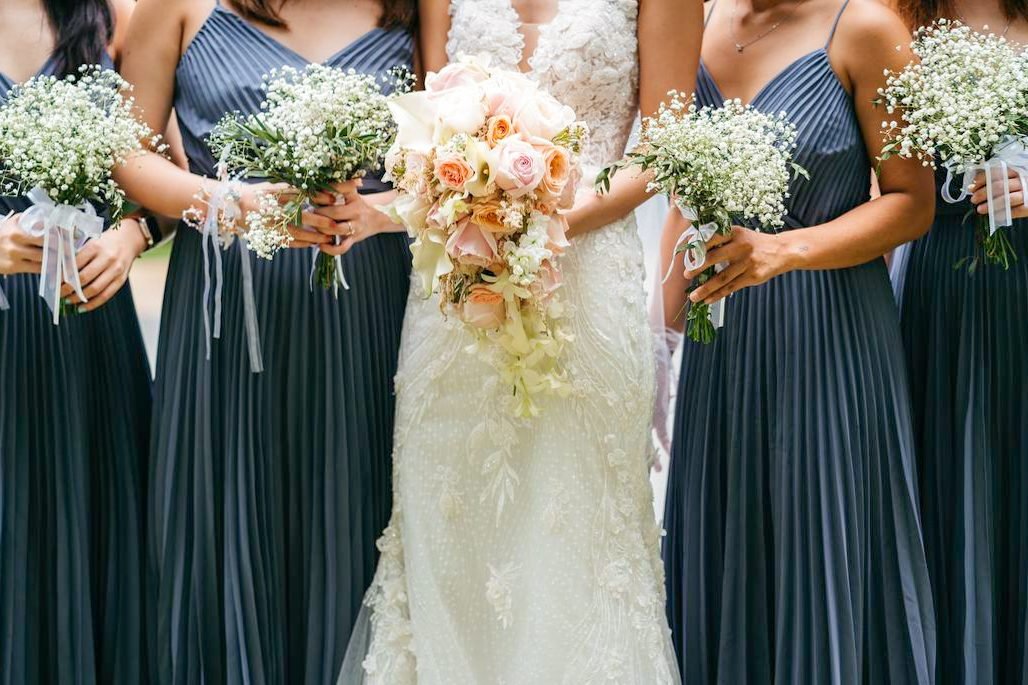 Bride with a peach and cream bouquet standing with bridesmaids holding white gypsophila posies