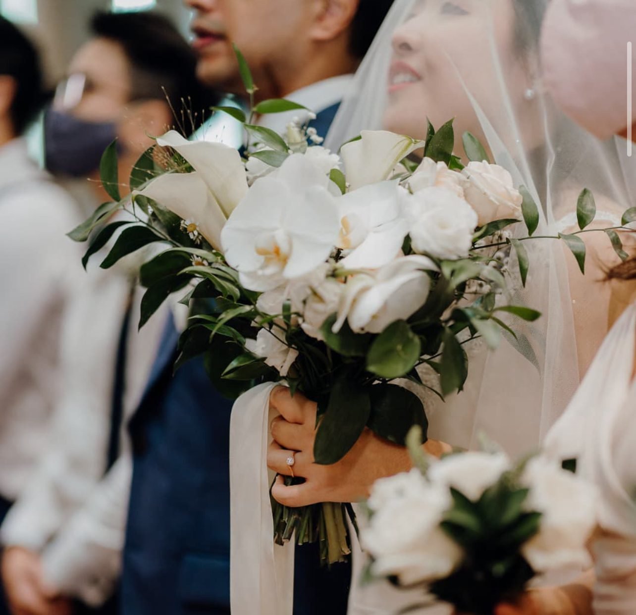 Close view of a white orchid and calla lily bouquet held by a veiled bride