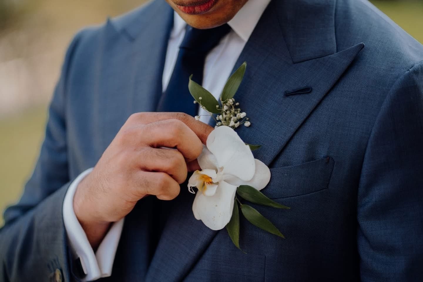 Groom in a navy suit adjusting a white orchid boutonniere