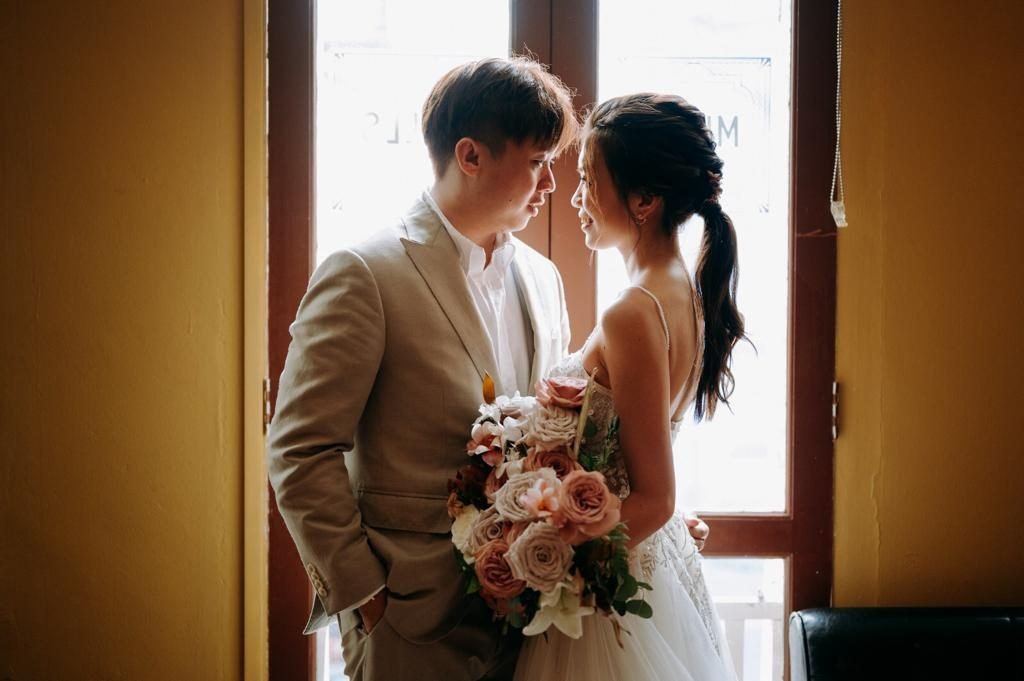 Couple standing by a window, the bride holding a dusty pink bouquet