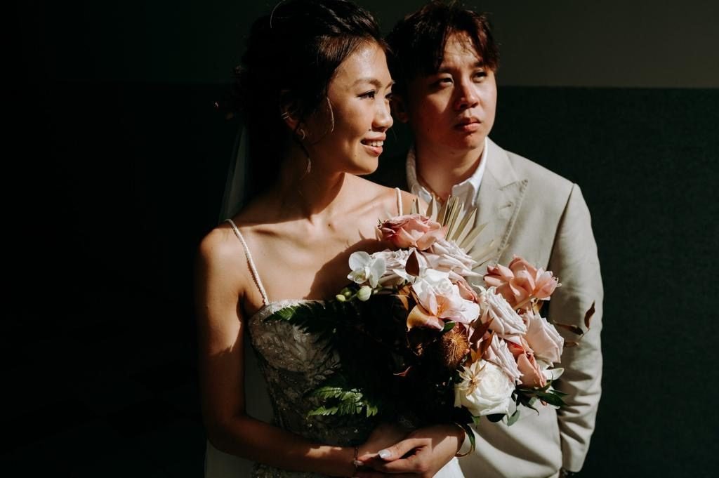 Couple against a dark wall, the bride holding a pink and white bouquet with dried foliage